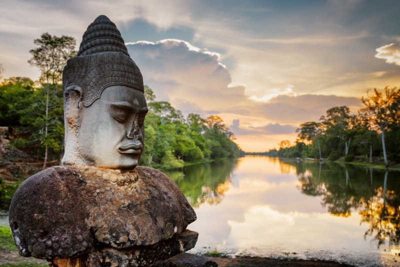 A stone figure beside calm water at Angkor in Cambodia